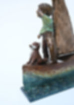 Close up Bronze boy in green jumper on patined boat with textured sail, and a fox sitting alert at his feet.
