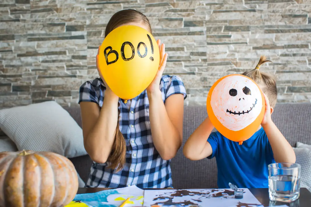 Two kids showing Halloween themed balloons. 