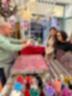 Artist demonstrates marbling technique to two women in a colourful workshop with star decorations. Various paint cups in foreground.