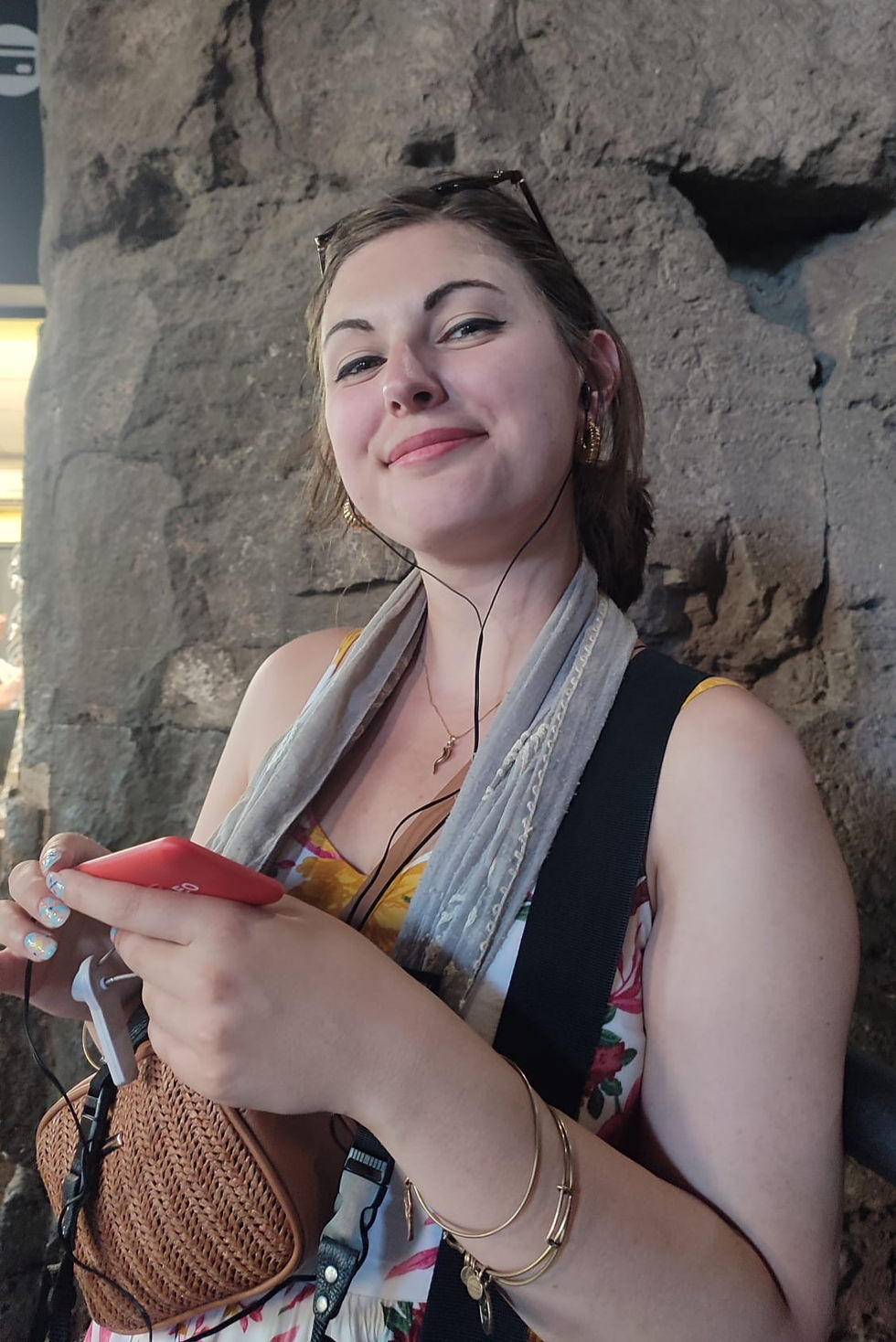 A woman smiles at the camera. She had a red audio guide in her hands and headphones in her ears.