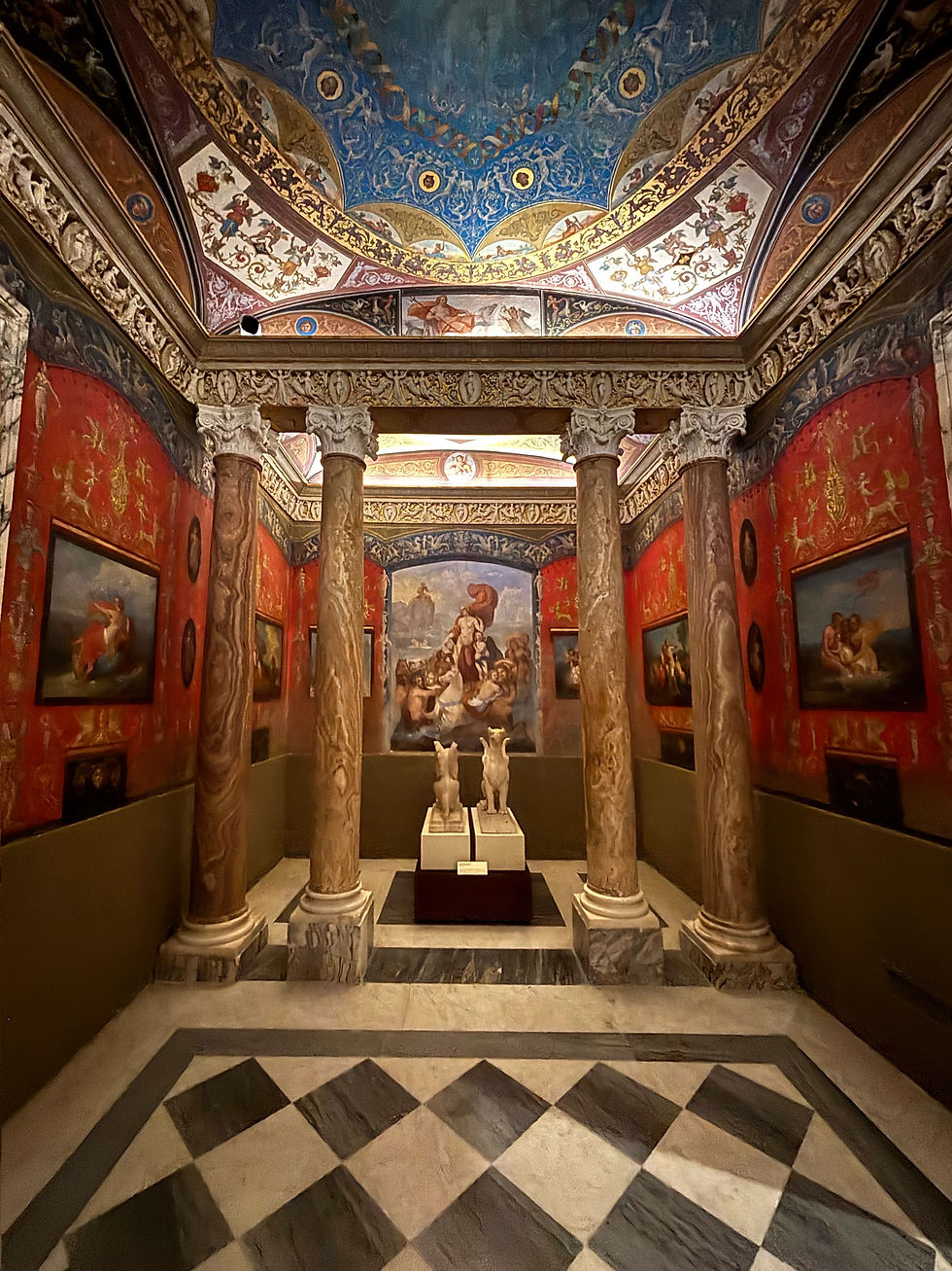 Ornate room with marble columns, red walls adorned with paintings, colorful detailed ceiling, and a central sculpture of two figures. Luxurious ambiance.