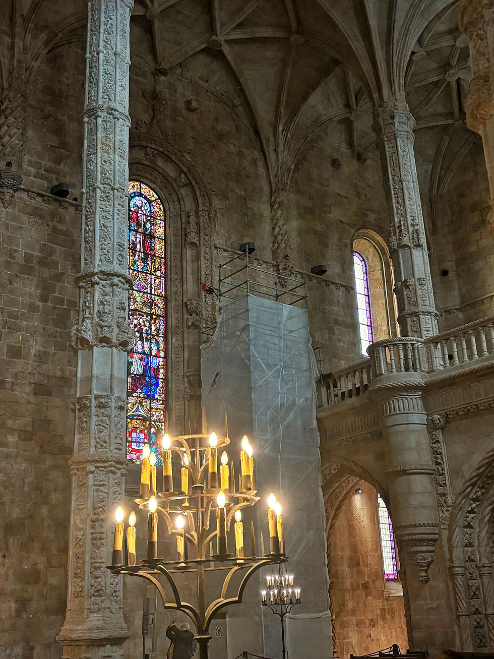 Ornate cathedral interior with tall carved columns, stained glass windows, lit candelabra, and scaffolding under stone vaults