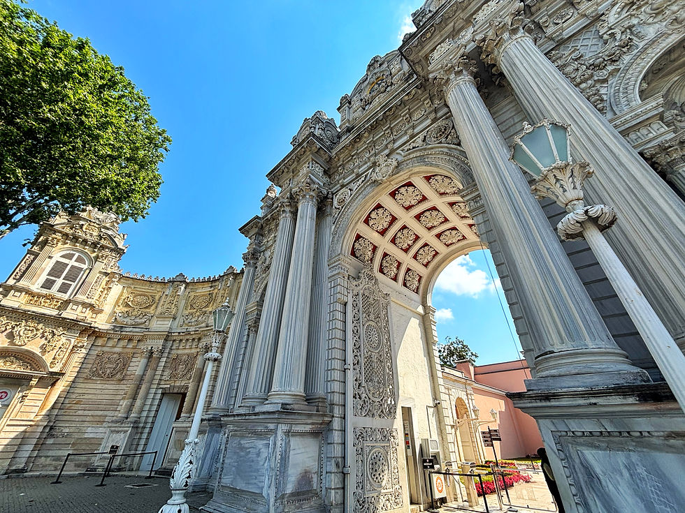 Ornate stone arch and columns of a grand historic building under a bright blue sky, with a leafy tree at left.