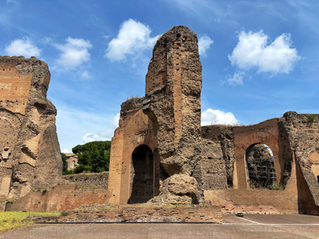 Ancient brick-and-stone ruins with arched openings under a bright blue sky with clouds, evoking a quiet, historical mood.