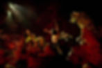 Multiple actors bathed in a red glow act on a rocky stage.
