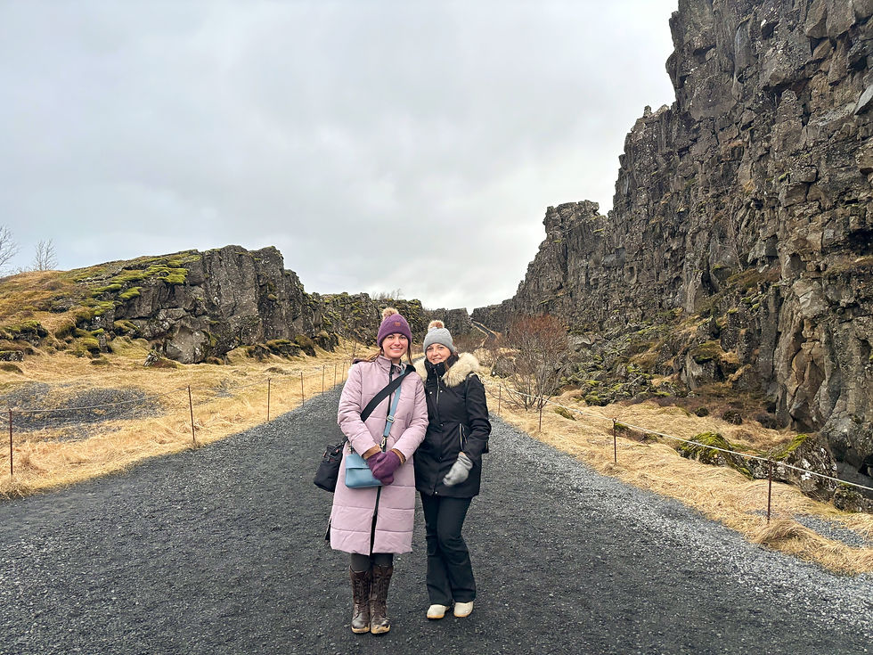 Two women stand on a lava stone path that is between two tectonic plates. The rock face on either side of them is very high.