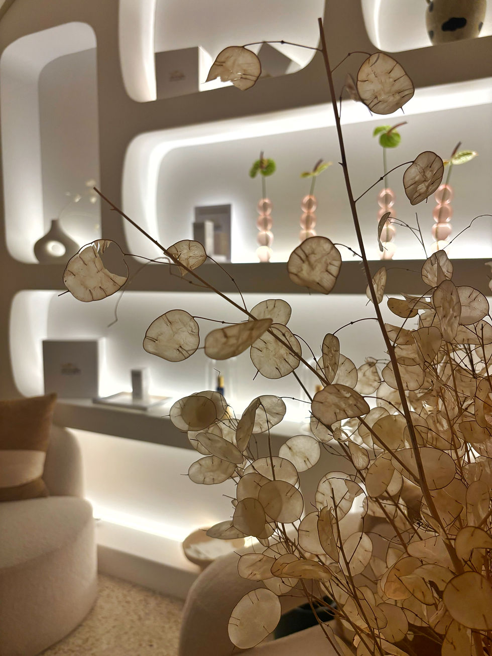 Dried leaves are in the foreground of a spa waiting room, with shelves in the back featuring flowers and various beauty products.