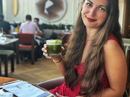 Smiling woman in a red dress holds a green cocktail at a restaurant table with napkins.