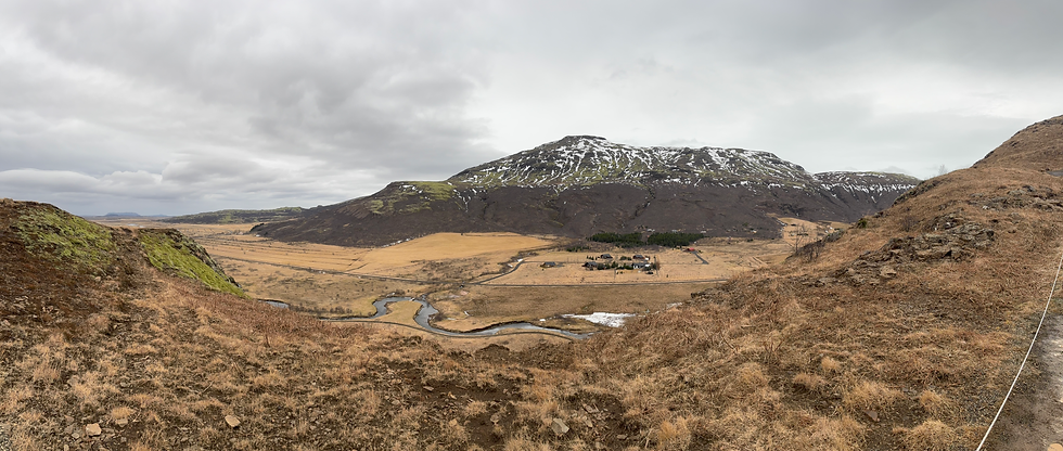 A small village in nestled in the mountains of Iceland's Golden Circle, with a large mountain in the back and a winding river in front of it. The land is brown and dry.