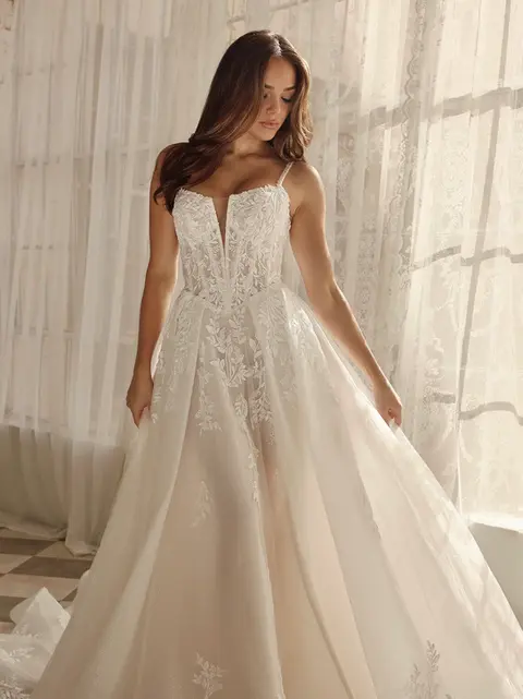 For the bride who dreams of a modern day fairytale, Style 1833 combines princess-inspired romance with a sexy, sophisticated edge. This romantic lace bridal gown features shimmering beaded spaghetti straps that connect to a sheer corset-style bodice and plunging notch neckline. Glittering beaded accents dance across leafy floral appliqué lace, cascading over the basque waistline and seamlessly transitioning into the full A-line skirt of glittering tulle, with pockets and a sexy leg slit for a modern touch. Available in both lined and unlined options for a customizable level of sheerness, the skirt flows into a delicate floating hemline complete with scattered floral lace appliqués to complete this romantic bridal gown. This sparkling princess wedding dress is also available in plus sizes.