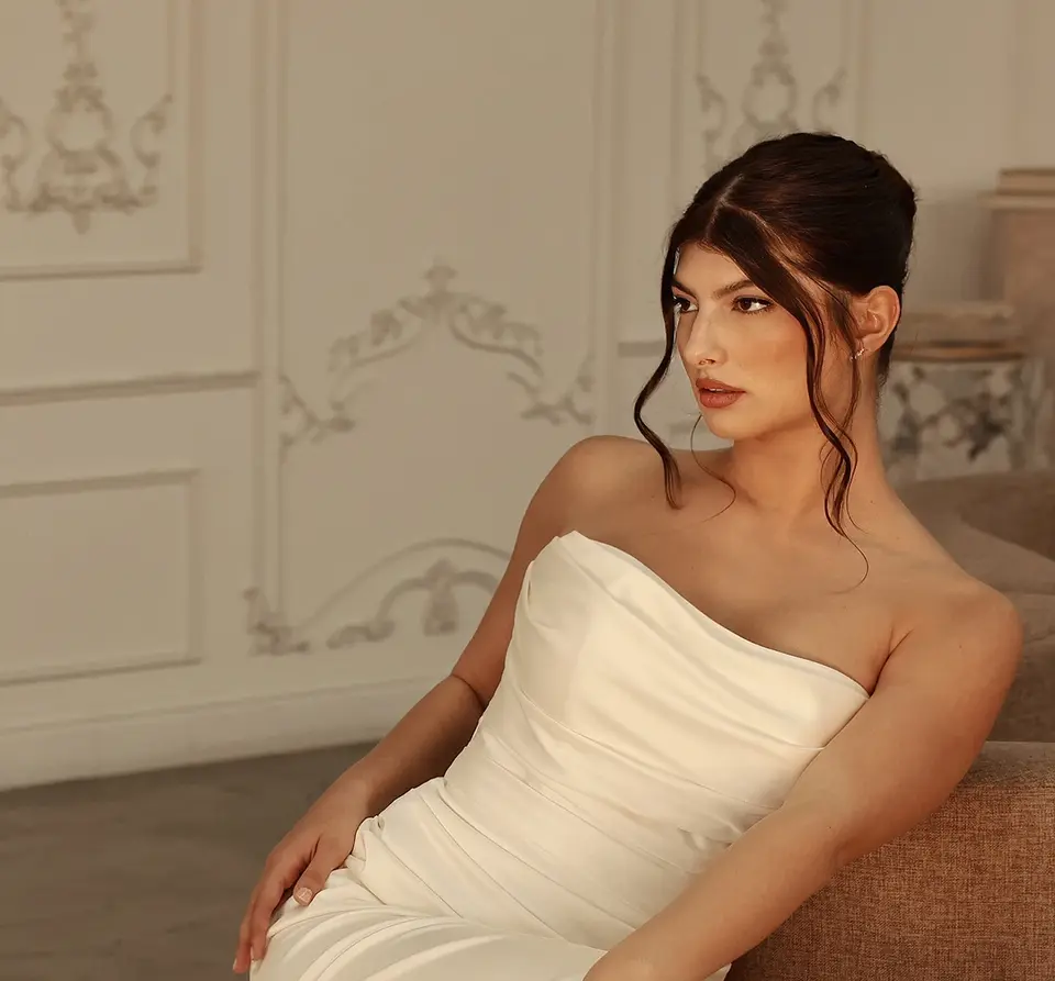 Modern Romantic Charmeuse Column Wedding Dress with Detachable Lace Sleeves and Train
Style 1874 is a modern column wedding dress in opulent charmeuse fabric featuring a detachable long sleeve lace topper and detachable lace train. The draped strapless bodice scoops at the neckline and wraps around the figure, ending with a gown-length row of fabric-covered buttons. The detachable lace topper with an elegant high neckline adds delicate floral lace to the bodice, extending the gown-length row of fabric-covered buttons down the back. The clean and chic column silhouette ruches at the back hip before flowing into a detachable lace train that cascades from a modern bow detail to complete this modern bridal look.