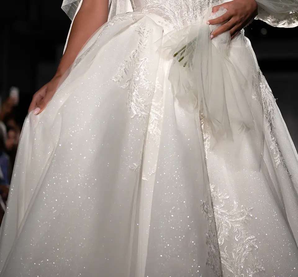 Strapless Sweetheart Princess Ballgown Wedding Dress with Glitter Tulle
Embroidered lace appliquƩs and shimmering glitter tulle come together in this romantic princess ballgown wedding dress. From a strapless sweetheart neckline, Style 1903's fitted bodice features intricate corset-style construction and a Basque waist beneath the scrolling filagree of beaded lace embellishments. In the back, the sparkling tulle shines as a row of pearl buttons elegantly close the back bodice. The voluminous ballgown skirt moves freely with each step and concludes with a lace-embellished train to complete this modern princess bridal gown.