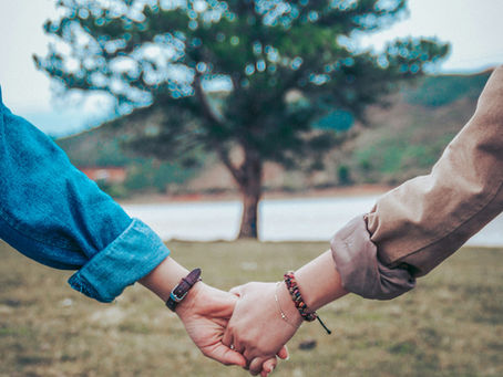 Two people holding hands in front of tree