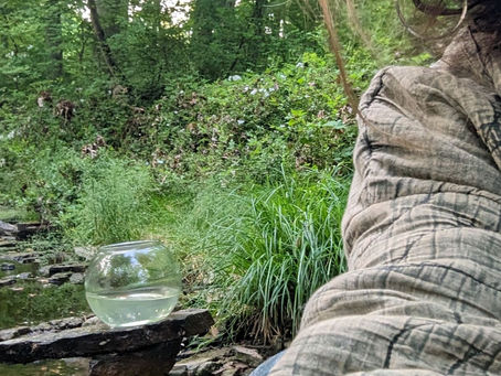 Artist photographing fish bowl on stacked stones out in nature