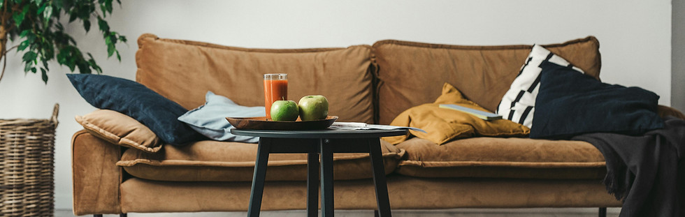 A messy brown sofa with many pillows and a coffe table in front of it