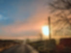 Sunset over a rural road with bare trees and power lines. Warm orange and blue sky creates a calm, serene mood.