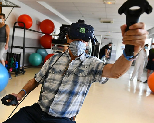 Un paciente se sienta en el área técnica de la clínica Les Rosiers en Dijon. Lleva unas gafas de realidad virtual terapéuticas y sostiene controladores. Realiza movimientos amplios.