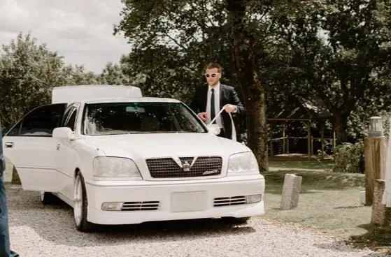 a man in a suit and tie is standing next to a white car .