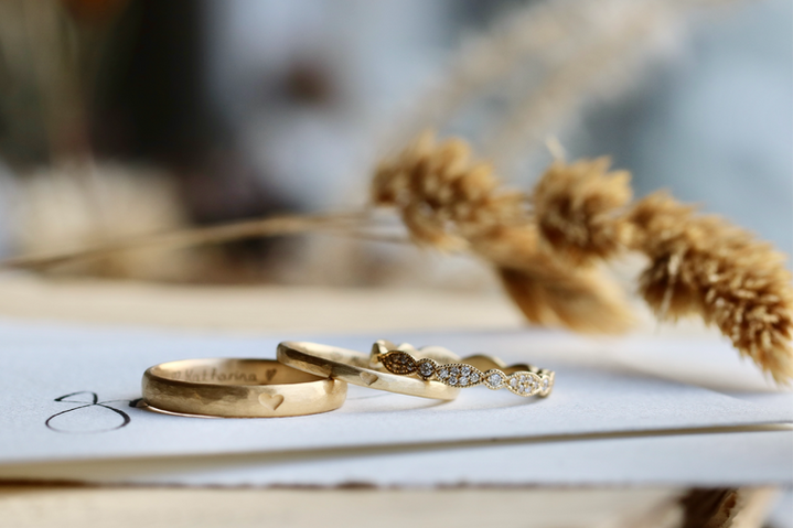 Recycled gold wedding ring set with engraved heart symbols and diamonds – consisting of one men's ring and two matching women's rings, photographed on paper with dried flowers.