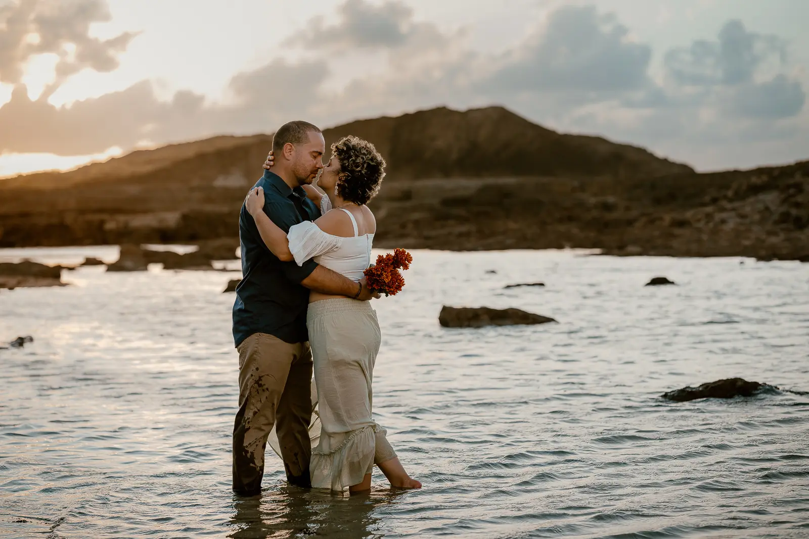 Couple at the beach with flowers kissing at sunset