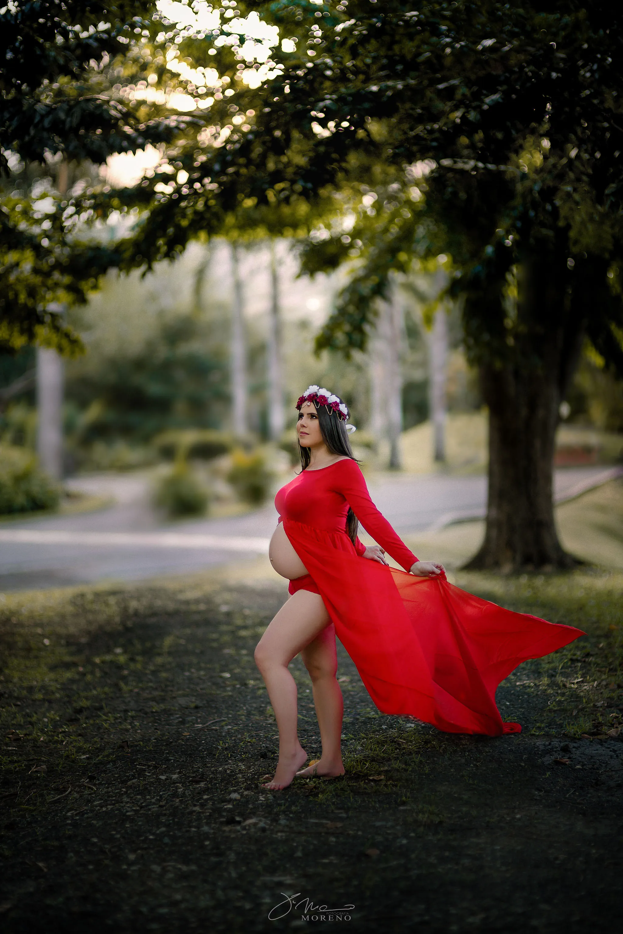 pregnant lady in a red dress with flying tale posing in the forest