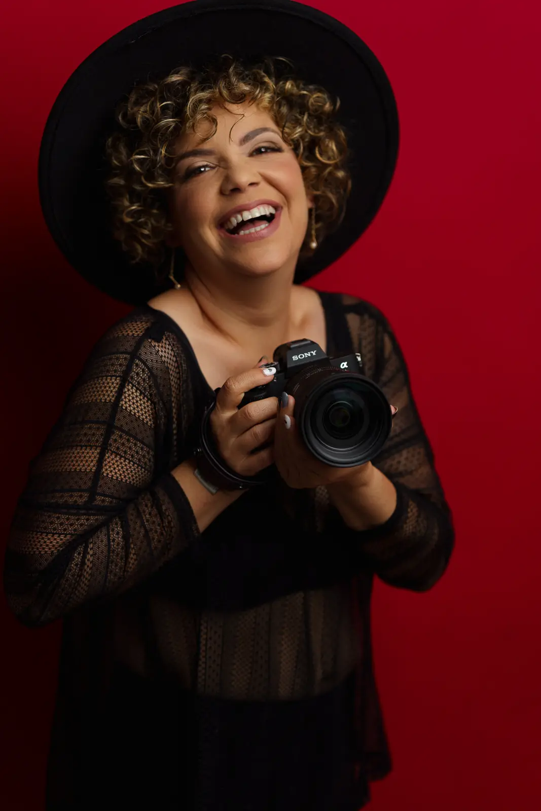 woman posing with sony camera in studio with red background and a hat
