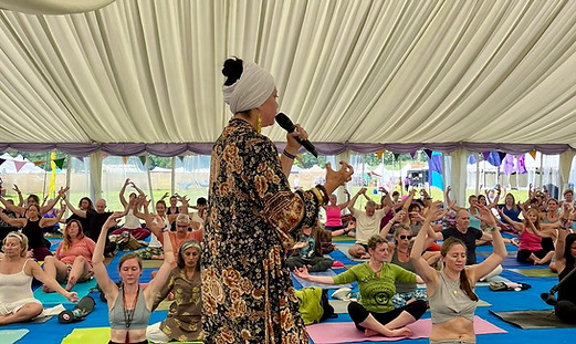 Thimela Garcia leading a large Kundalini Yoga festival workshop inside a wellness tent, guiding participants through meditation, breathwork and movement practices