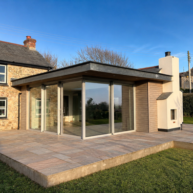 Contemporary timber-clad and glazed extension to a traditional Cornish stone cottage, creating a bright connection to the garden