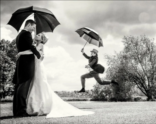Wedding couple under umbrella with jumping groomsman.