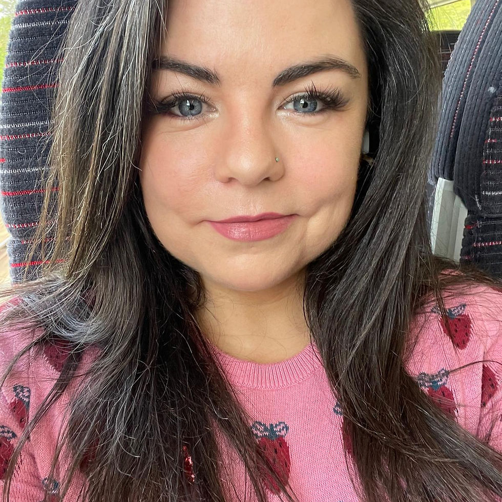 A picture of Kate O'Leary the blog author. She has long dark hair and pink lipstick smiles in a close-up. Wearing a pink sweater with strawberry print.