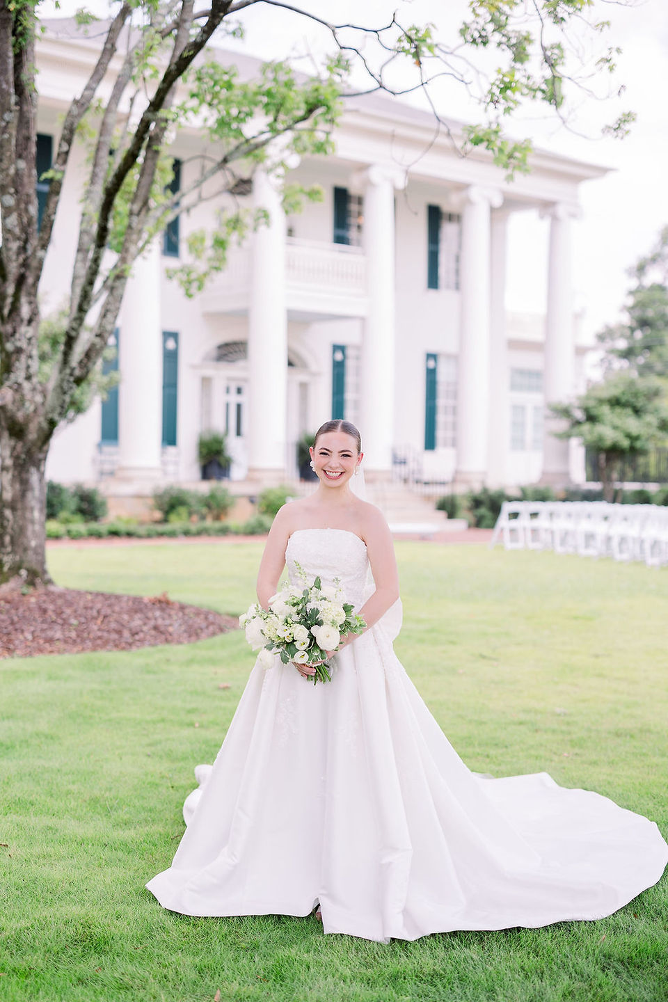 The bride stands with the venue in the background, smiling and holding her bouquet (Photo by Kara Beth Carr Photography)