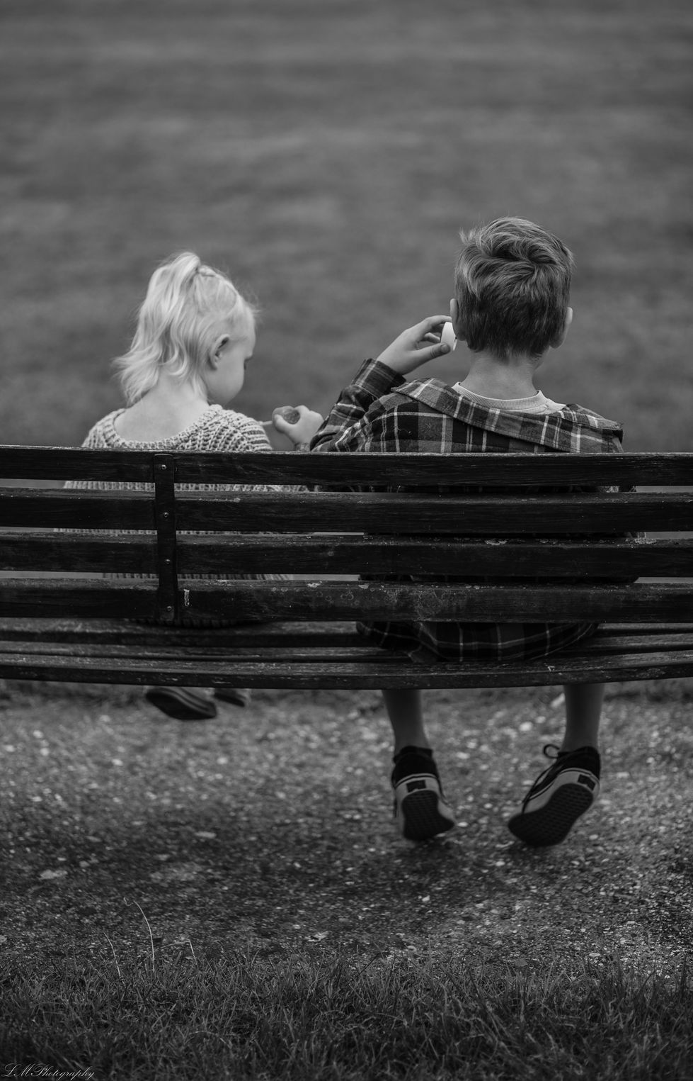 a boy and a girl sit on a park bench
