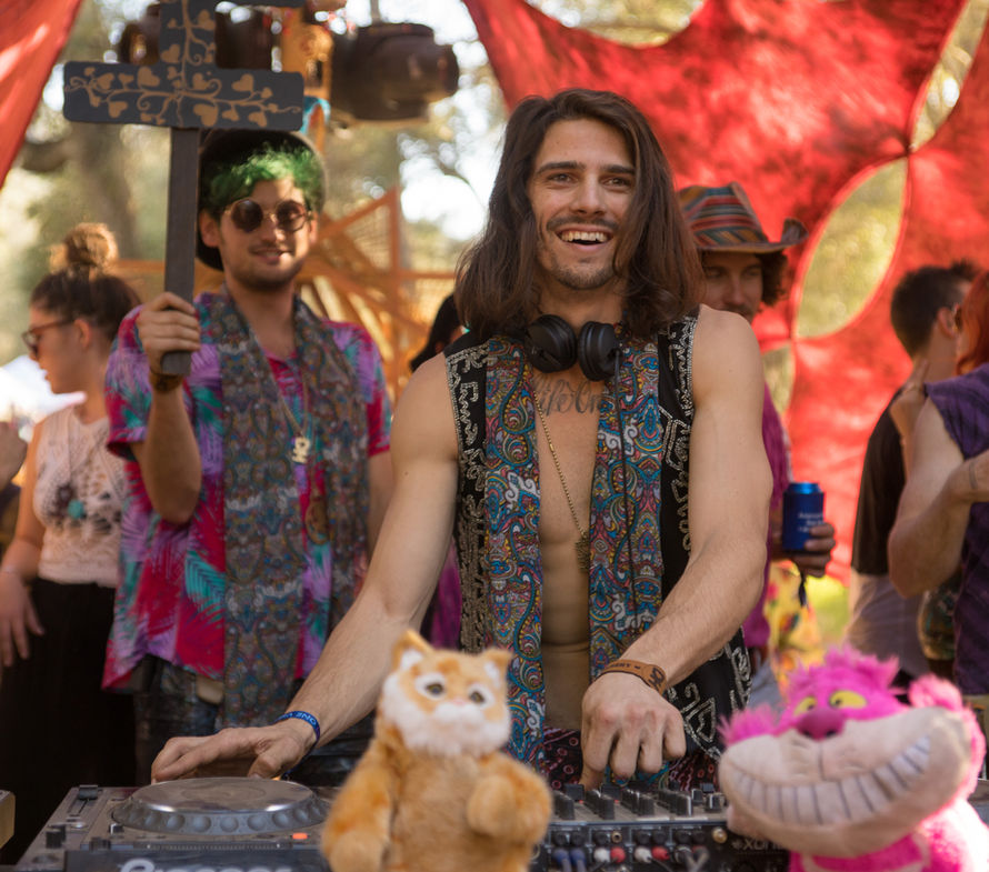 Two DJs playing together in front of a red patterned backdrop
