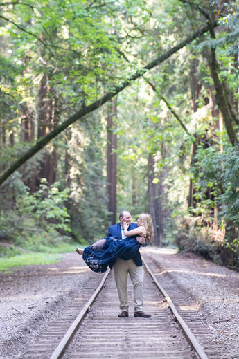 Man carrying his fiancée along railroad tracks through the redwoods