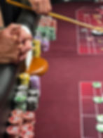 Hands arrange colorful casino chips beside a wooden roulette wheel on a red gaming table.