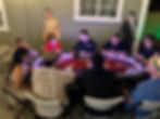 A casino dealer hosts a poker game for guests gathered around a red table on a patio.