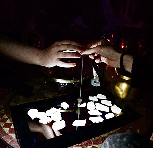 two hands hold a pendulum over a mirror with paper fragments in some form of ritual, from queens of the underworld's ZODIAC project