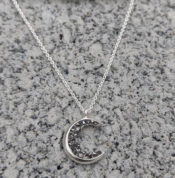 Silver crescent moon necklace on a textured gray background, close-up shot.