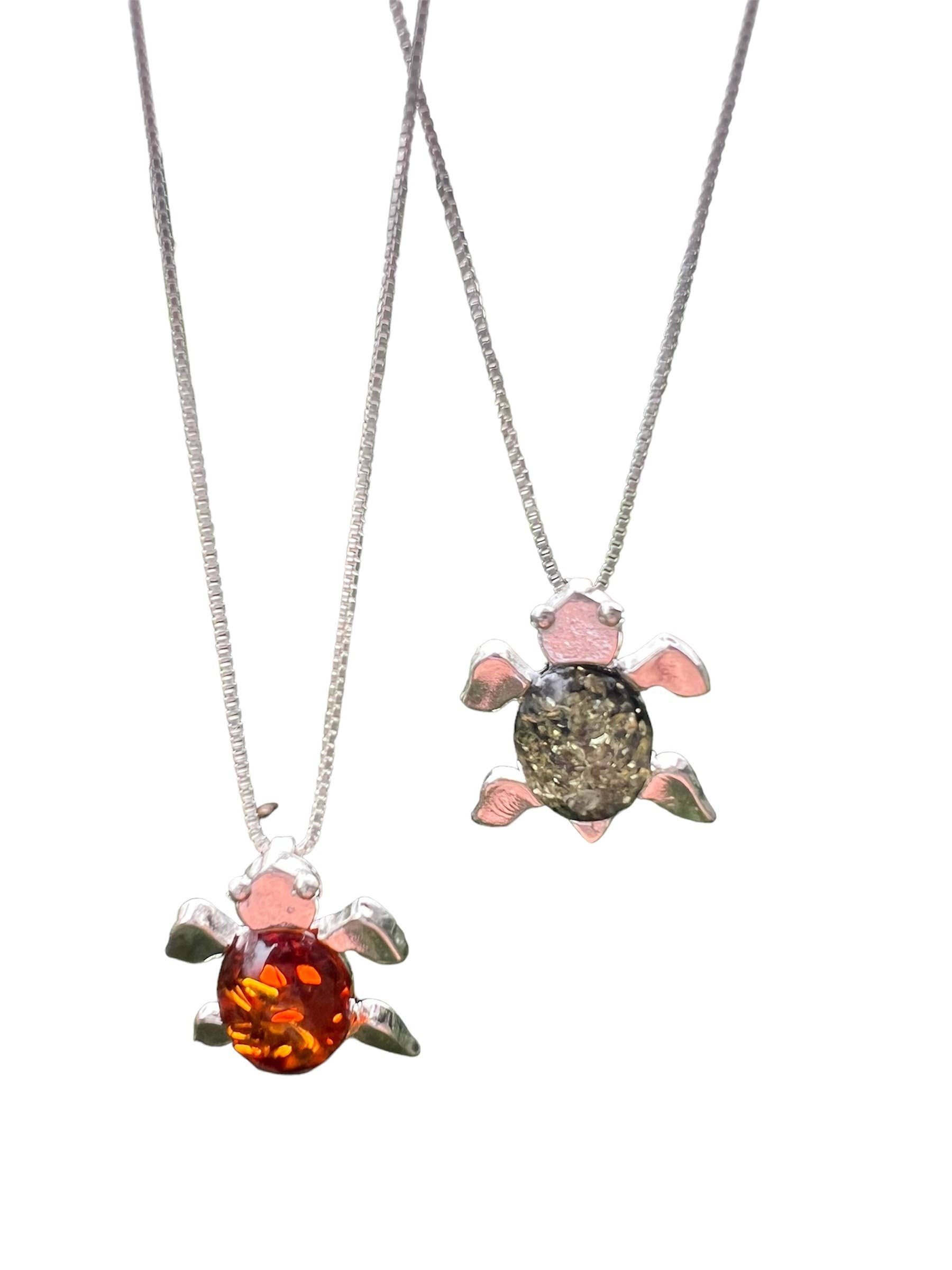Two turtle pendant necklaces with amber and black center stones, white background.
