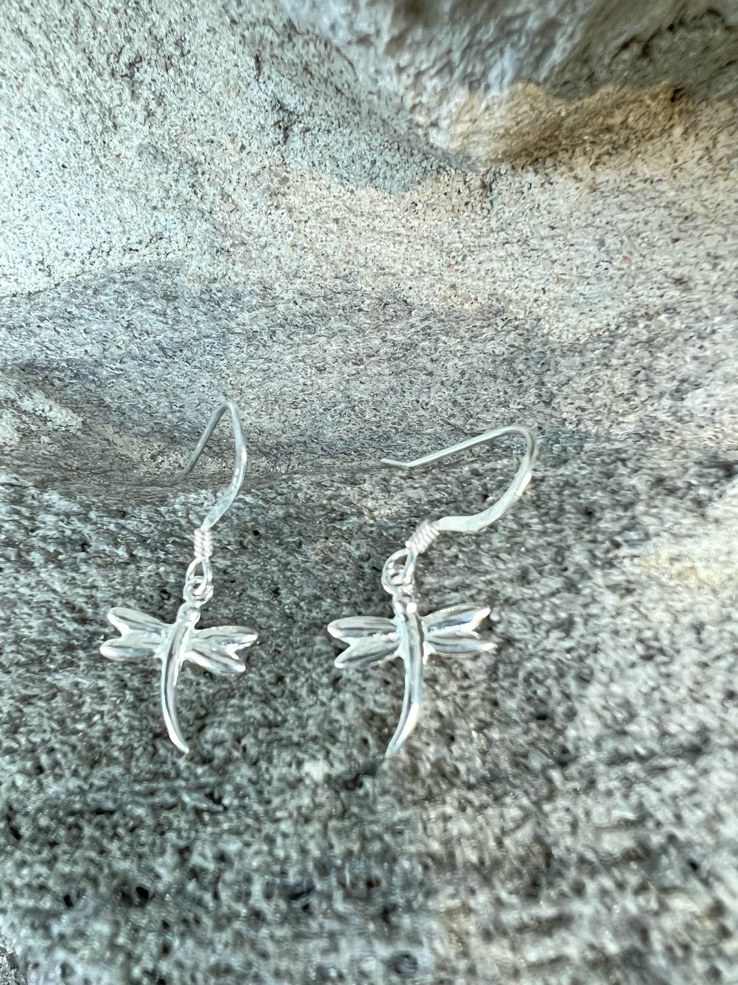 Silver dragonfly earrings on a textured background, elegant and close-up view.