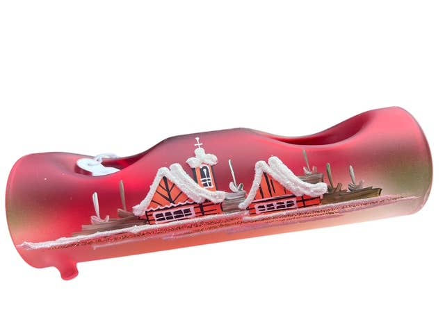 Red glass art with a village scene, white snow, and unique shape.