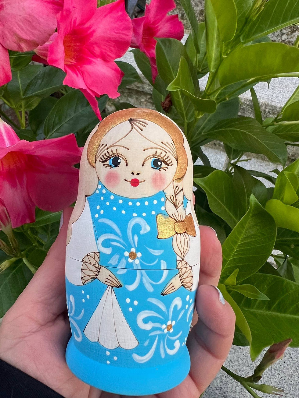 Thumbnail: Hand holding a LARGE BLUE Floral Nesting Dolls Set, 7 pcs/9" against pink flowers