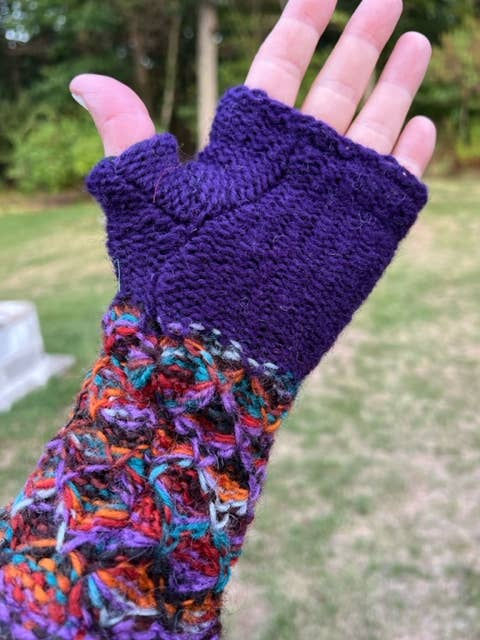 Hand wearing a purple fingerless glove with colorful textured wristband outdoors.