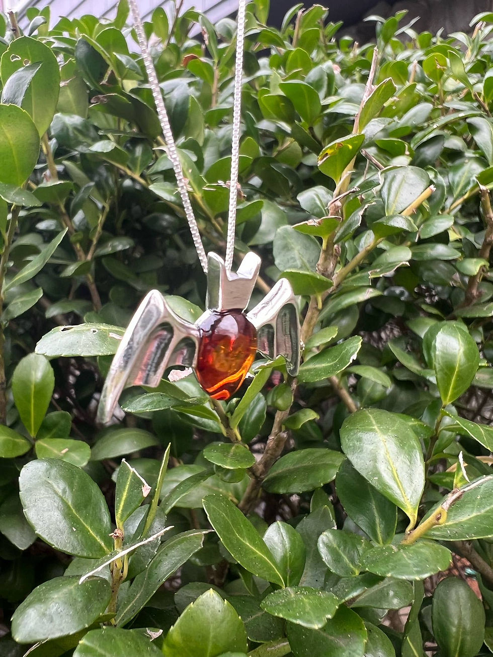 Thumbnail: Silver necklace with amber pendant, set against green shrubbery backdrop.