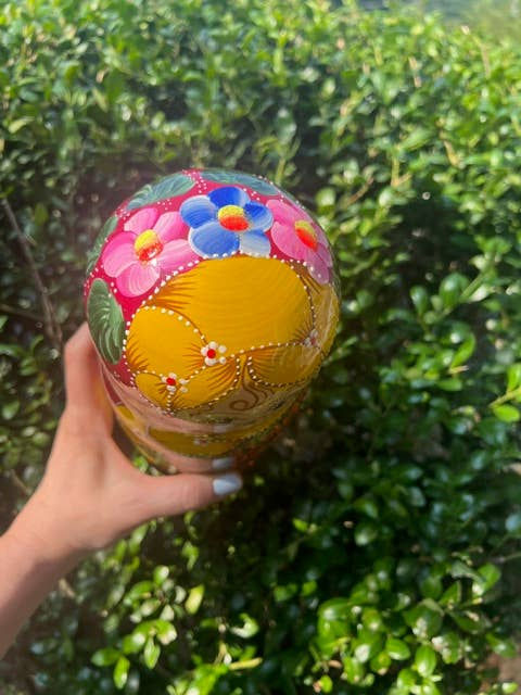 Thumbnail: Hand holding a LIGHT GREEN Floral Nesting Dolls Set, 5 Pcs/6" with colorful flowers, outdoors.