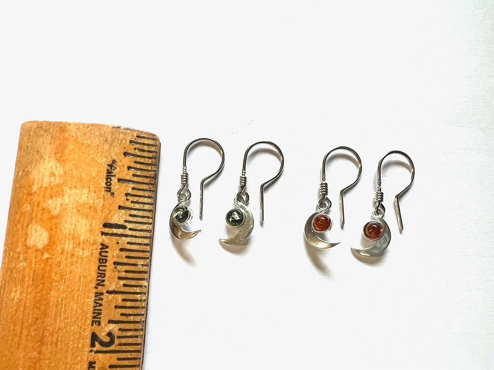 Four pairs of earrings beside a ruler on a white surface.