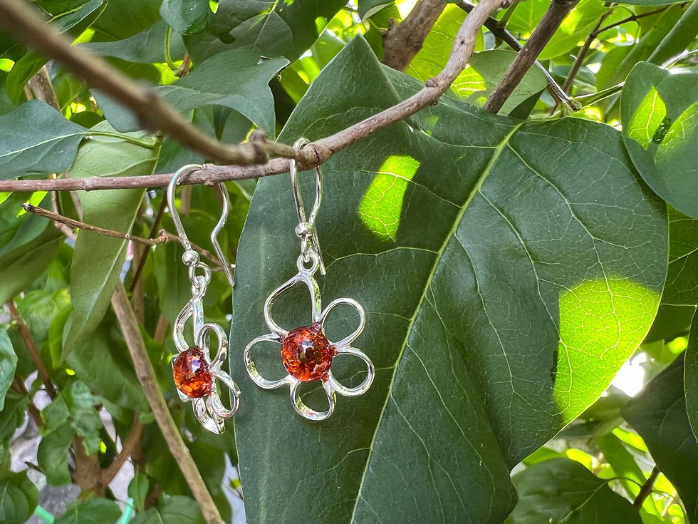 Thumbnail: Floral silver earrings with orange gem stones hanging on a leafy branch