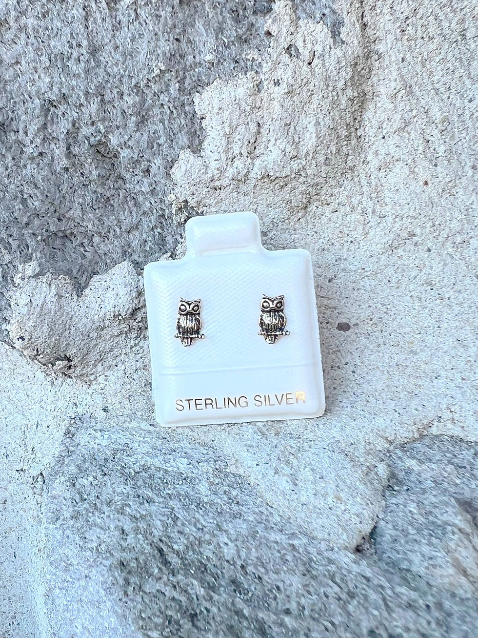 Pair of sterling silver owl earrings on a display card, close-up shot.