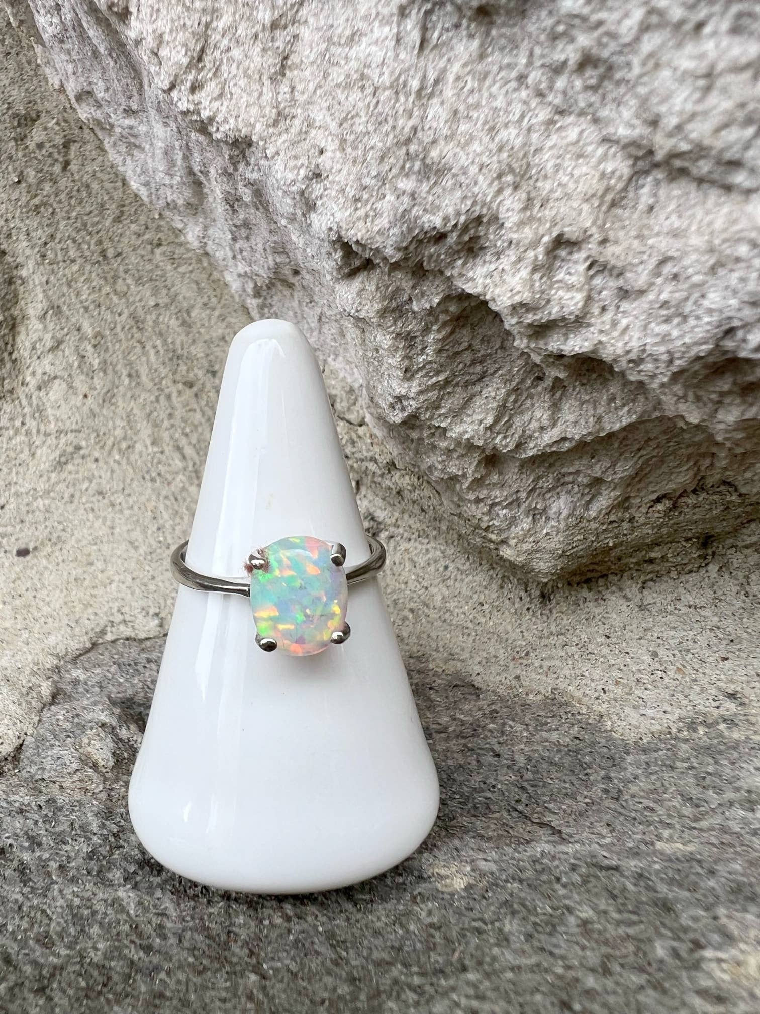 Silver ring with opal gem on white cone, natural stone background.
