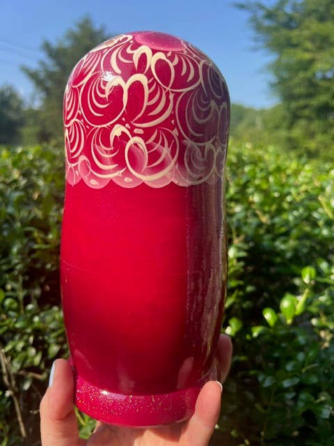 Thumbnail: Red floral nesting doll held up in front of green background.